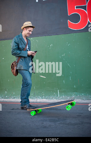 Metà maschio adulto guidatore di skateboard la lettura di un messaggio di testo sullo smartphone Foto Stock