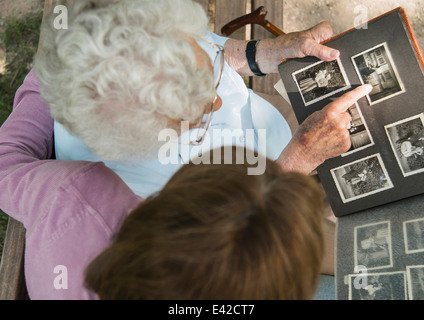 Senior donna seduta su una panchina nel parco con il nipote, guardando vecchi album di foto Foto Stock