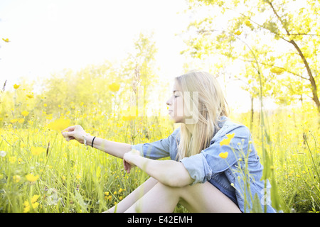 Giovane donna seduta in campo con fiori di campo Foto Stock