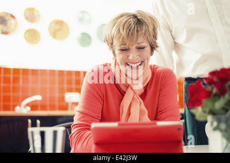 Donna matura con tavoletta digitale in cucina Foto Stock