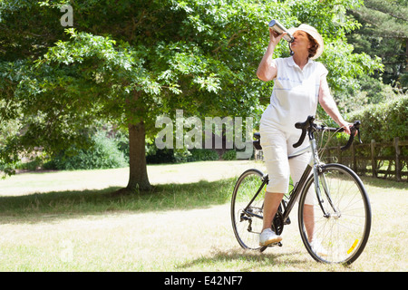 Senior donna ciclista acqua potabile in posizione di parcheggio Foto Stock