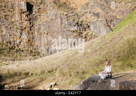 Giovane donna in posizione di yoga sul lago rock Foto Stock