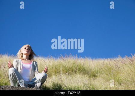 Giovane donna in posizione di yoga sulla collina erbosa Foto Stock