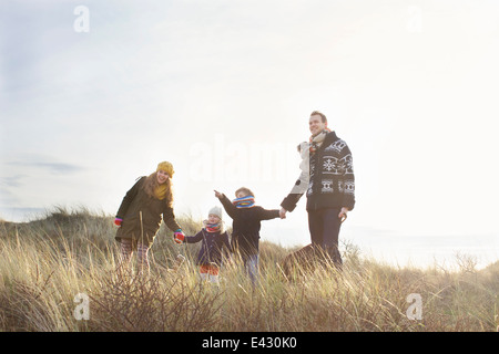 Metà adulto giovane in piedi in dune di sabbia con il loro figlio, figlia e cane Foto Stock