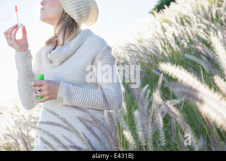 Ritagliato shot della giovane donna a soffiare bolle in erba lunga Foto Stock