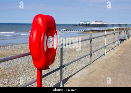 Lifebelt sul lungomare a Cromer, Norfolk. Pier e stazione di salvataggio in background. Foto Stock