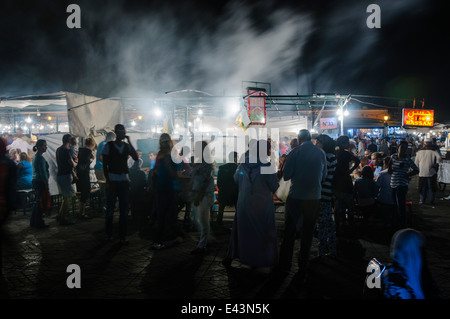 La folla si riuniranno presso chioschi in piazza Jemaa El-Fná Fnaa (Piazza Grande) di notte a Marrakech, Marocco Foto Stock