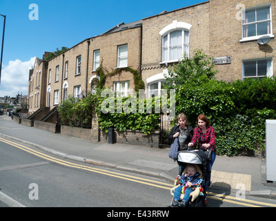 Due donne di strada di attraversamento con il bambino nel passeggino e alloggiamento in Shacklewell Lane Dalston Hackney East London E8 KATHY DEWITT Foto Stock