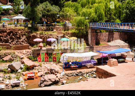 Patio in plastica tavoli, sedie e ombrelloni presso i ristoranti sulle rive del fiume Ourika, Ourika Valley, Atlante, Marocco Foto Stock