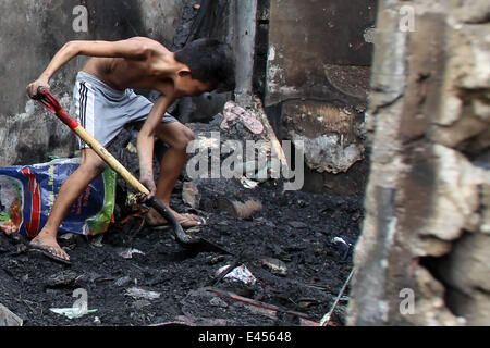 Mandaluyong City, Filippine. 3 Luglio, 2014. Un ragazzo cerca materiali riutilizzabili dopo un incendio ha colpito una zona residenziale in Mandaluyong City, Filippine, il 3 luglio 2014. Il fuoco ha lasciato più di cento abitanti senzatetto e una ragazza muore in un incidente. Credito: Rouelle Umali/Xinhua/Alamy Live News Foto Stock