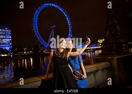 Due giovani amici di sesso femminile prendendo ritratto di auto di notte, Londra, Regno Unito Foto Stock