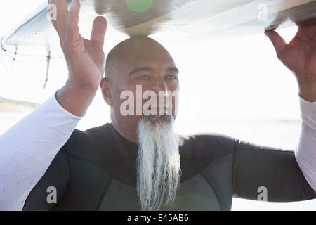 Chiusura del maschio maturo di bilanciamento del surfista con la tavola da surf sulla testa Foto Stock