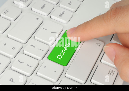 Mano verde di spinta donare il pulsante sulla tastiera bianca Foto Stock