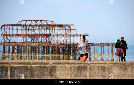 Brighton, Sussex, Regno Unito. 4 Luglio, 2014. Una giovane donna corre davanti al Molo Ovest sul lungomare di Brighton questa mattina come le temperature erano attese per raggiungere 29 gradi centigradi nel Sud Est più tardi di oggi Foto Stock