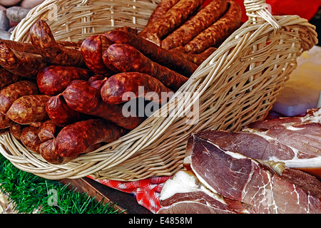 Salsicce tradizionali collocati in un cesto di vimini, prosciutto e pancetta tagliata per essere servito. Foto Stock