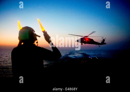 US Navy sailor segnali per i piloti in un MH-60S Sea Hawk elicottero a terra sul ponte di volo dell'guidato-missile destroyer USS Arleigh Burke durante la notte il rifornimento del 20 giugno 2014 nel Mare Arabico. Foto Stock