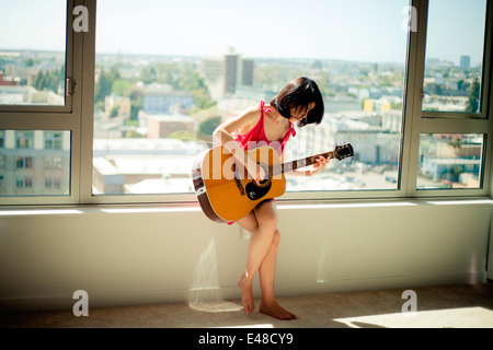 Giovane donna seduta sul davanzale e suonare la chitarra Foto Stock