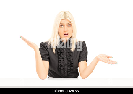 Confuso donna gesti con le mani seduti a un tavolo Foto Stock