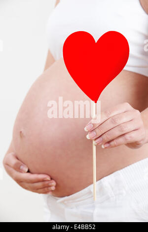 Close up della Donna Incinta Azienda forma di cuore Foto Stock