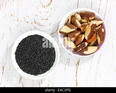 Due ciotole di semi di papavero e noci del Brasile su un bianco sullo sfondo di legno Foto Stock