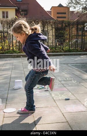 Ragazza bionda giocando campana sul marciapiede, Monaco di Baviera, Germania Foto Stock