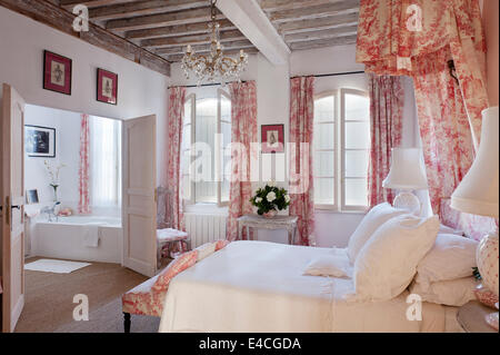 Rosa e Bianco toile de jouy sui cuscini, tende e letto baldacchino coronet in camera da letto con travi di legno a vista e il monitor al posto letto Foto Stock