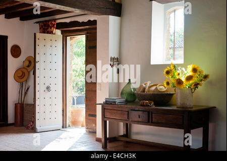 Brocca di girasoli sulla vecchia console in legno tabella nella hall di entrata costellato di porta e pavimento in piastrelle di terracotta Foto Stock