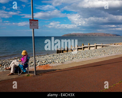 Donna rilassante sulla sedia a sdraio sulla spiaggia di Ross on Wye a Conwy North Wales UK con il Great Orme e Llandudno in distanza Foto Stock