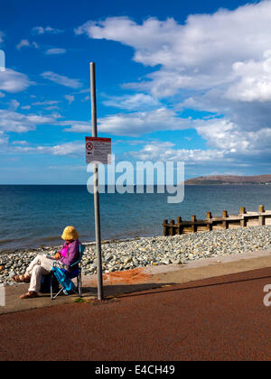 Donna rilassante sulla sedia a sdraio sulla spiaggia di Ross on Wye a Conwy North Wales UK con il Great Orme e Llandudno in distanza Foto Stock