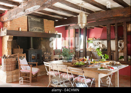 Grande francese rustica cucina di paese con le vecchie travi a soffitto, woodburning stufa e prevista tabella Foto Stock