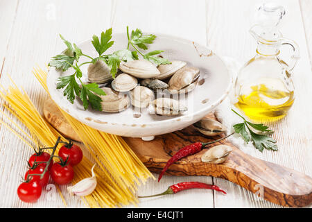 Gli ingredienti per cucinare gli spaghetti vongole gusci vongole, raw spaghetti, prezzemolo in foglie, di pomodori ciliegini Foto Stock