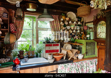 Il lavandino in shabby chic cucina di paese con la Cina che abbelliscono ogni superficie e un orologio del nonno nell'angolo Foto Stock