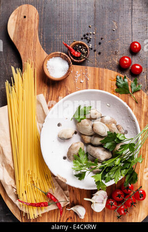 Gli ingredienti per cucinare gli spaghetti vongole gusci vongole, materie sapaghetti, prezzemolo in foglie, di pomodori ciliegini Foto Stock