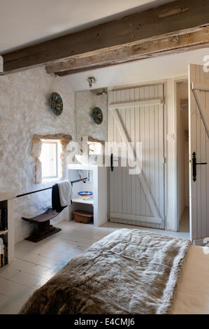 Pietra camera con soffitto con travi in legno a vista, lavabo e pelliccia buttare sul letto Foto Stock