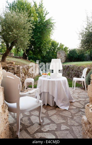 White fauteuil poltrona sulla terrazza in pietra con tavolo da pranzo e lampada da tavolo tutti dal Piccione D'Or Foto Stock