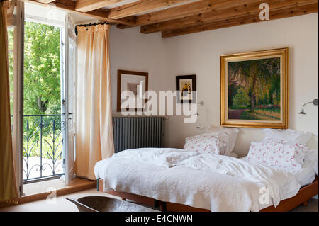 Dorato paesaggio incorniciato dipinto sulla parete di una camera da letto con travi a vista sui soffitti e finestre alla francese con vista sul giardino Foto Stock