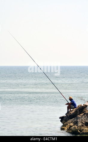 Pescatore solitario con una lunga asta sulle rocce al Coral Bay, Cipro Foto Stock