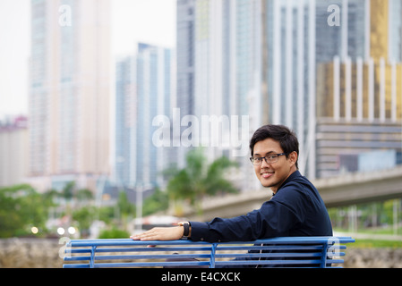 Ritratto di imprenditore cinese di sedersi e rilassarsi sulla panchina in Panama city con skyline e edifici per uffici in background Foto Stock