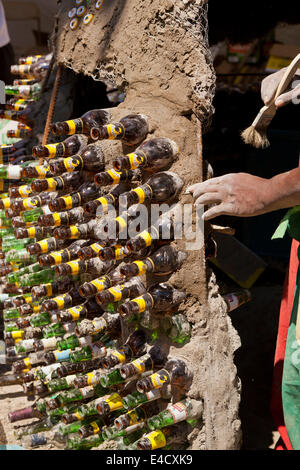 Uomo keniano costruire una capanna di fango con bottiglie di vetro e di altri materiali riciclati Foto Stock