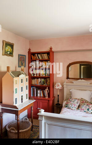 Vecchia casa delle bambole sul piano di marmo lavandino in camera da letto con il libro rosso di ripiano e bianco letto in legno Foto Stock