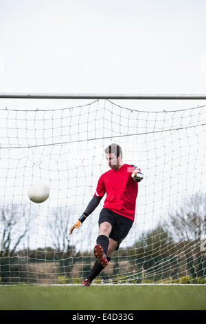 Il portiere in rosso calci palla lontano da obiettivo Foto Stock