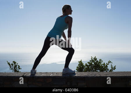 Montare donna stretching le gambe guardando al mare Foto Stock