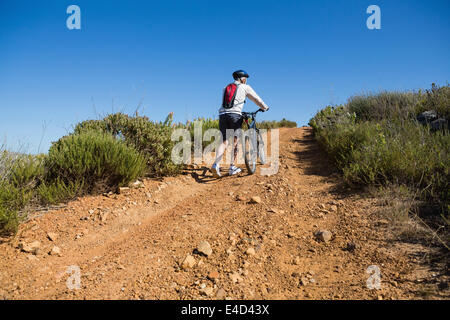 Montare il ciclista spingendo in salita in bicicletta sul terreno del paese Foto Stock