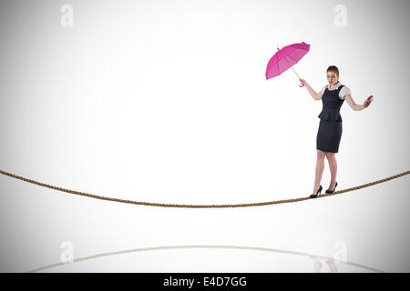 Immagine composita di pretty redhead imprenditrice azienda ombrello sul tightrope Foto Stock