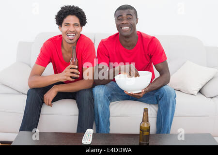 Per gli appassionati di calcio in rosso seduto sul divano con birra e pop corn Foto Stock