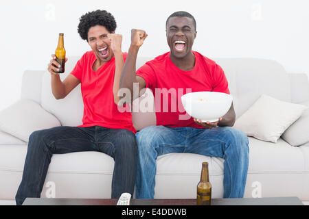 Per gli appassionati di calcio in rosso seduto sul divano con birra e pop corn Foto Stock