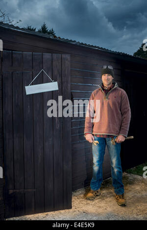 Uomo in piedi al di fuori della sua officina strumenti di contenimento. Foto Stock