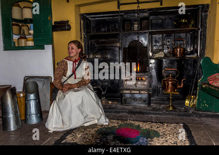 Giovane donna in costume seduto davanti a un caminetto Black-Leaded con carbone botole, Rag tappeto sul pavimento Foto Stock