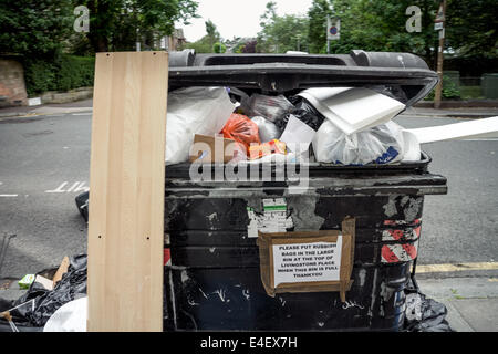 Grande comunale nero bidone con ruote traboccante di spazzatura in Edinburgo area Marchmont Foto Stock