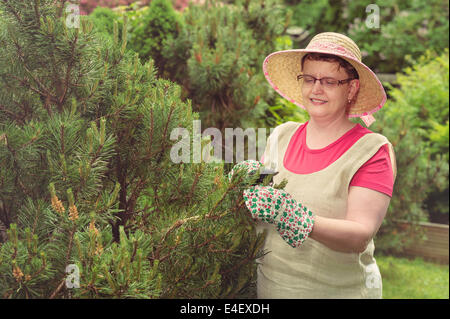 Donna matura utilizzare le forbici per potatura in giardino, croce immagine elaborata Foto Stock